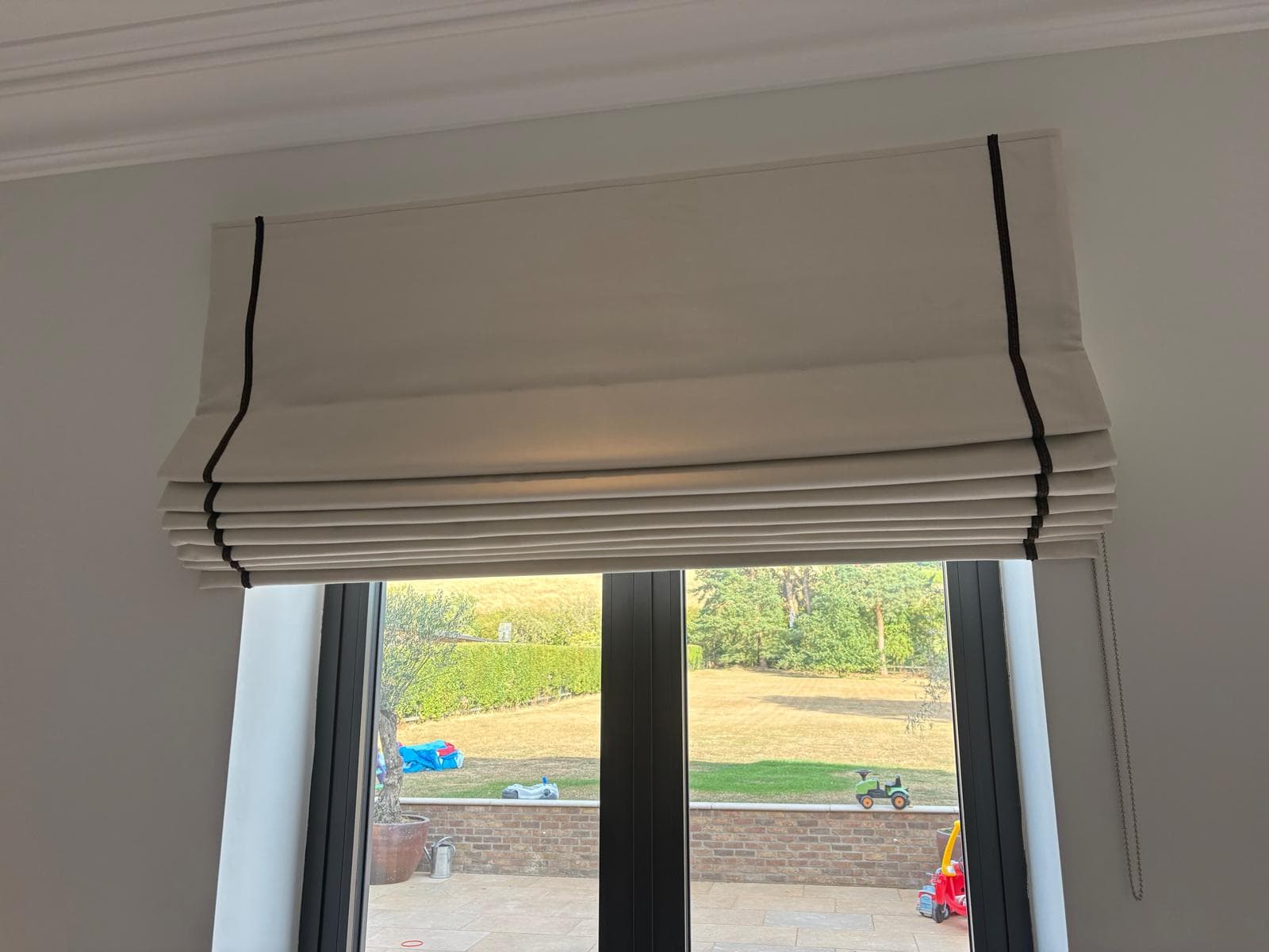 Cream roman blind with a dark contrast braid, fitted above garden doors