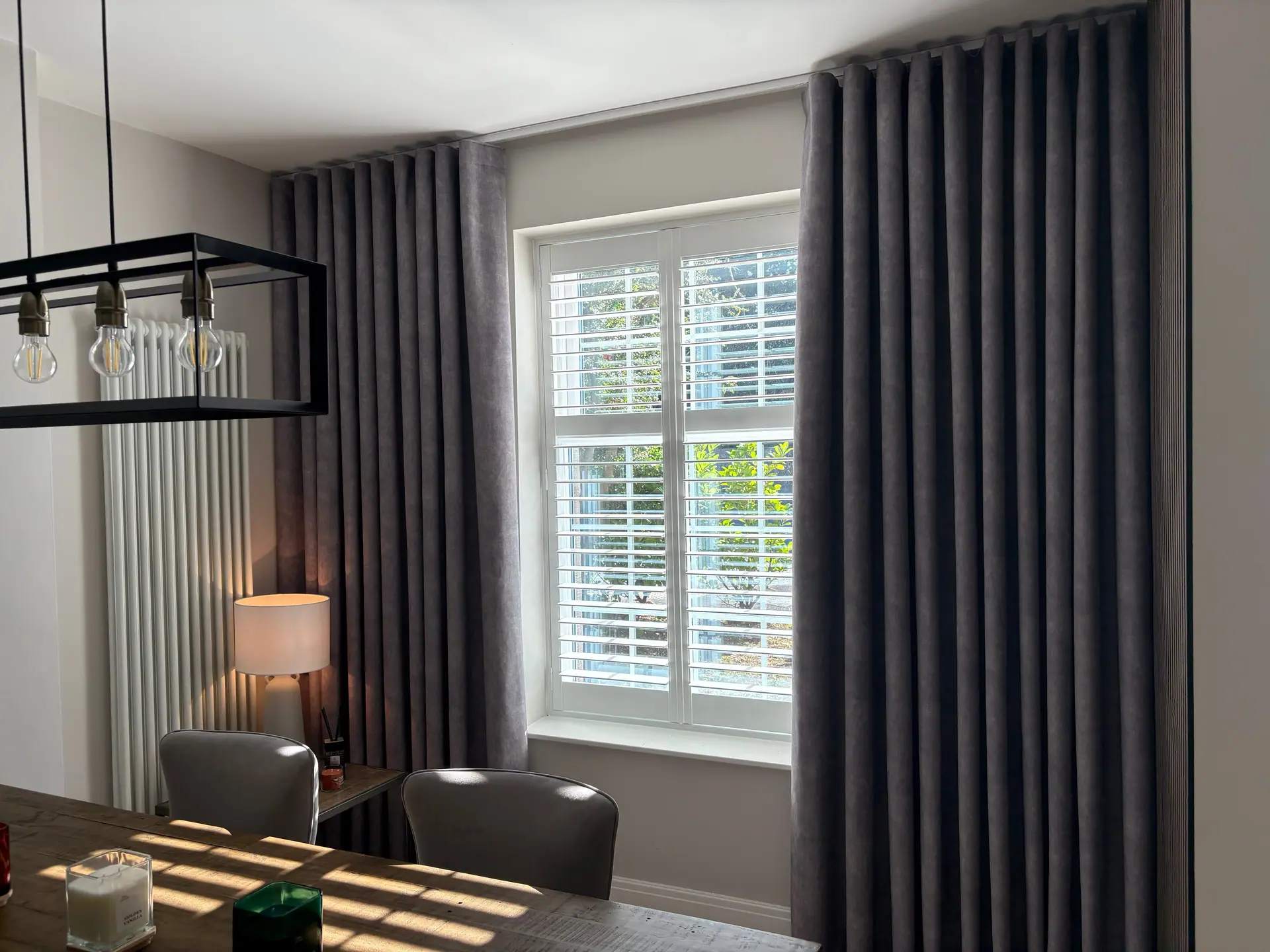 Deep grey wave-heading curtains either side of a window fitted with white tier-on-tier shutters